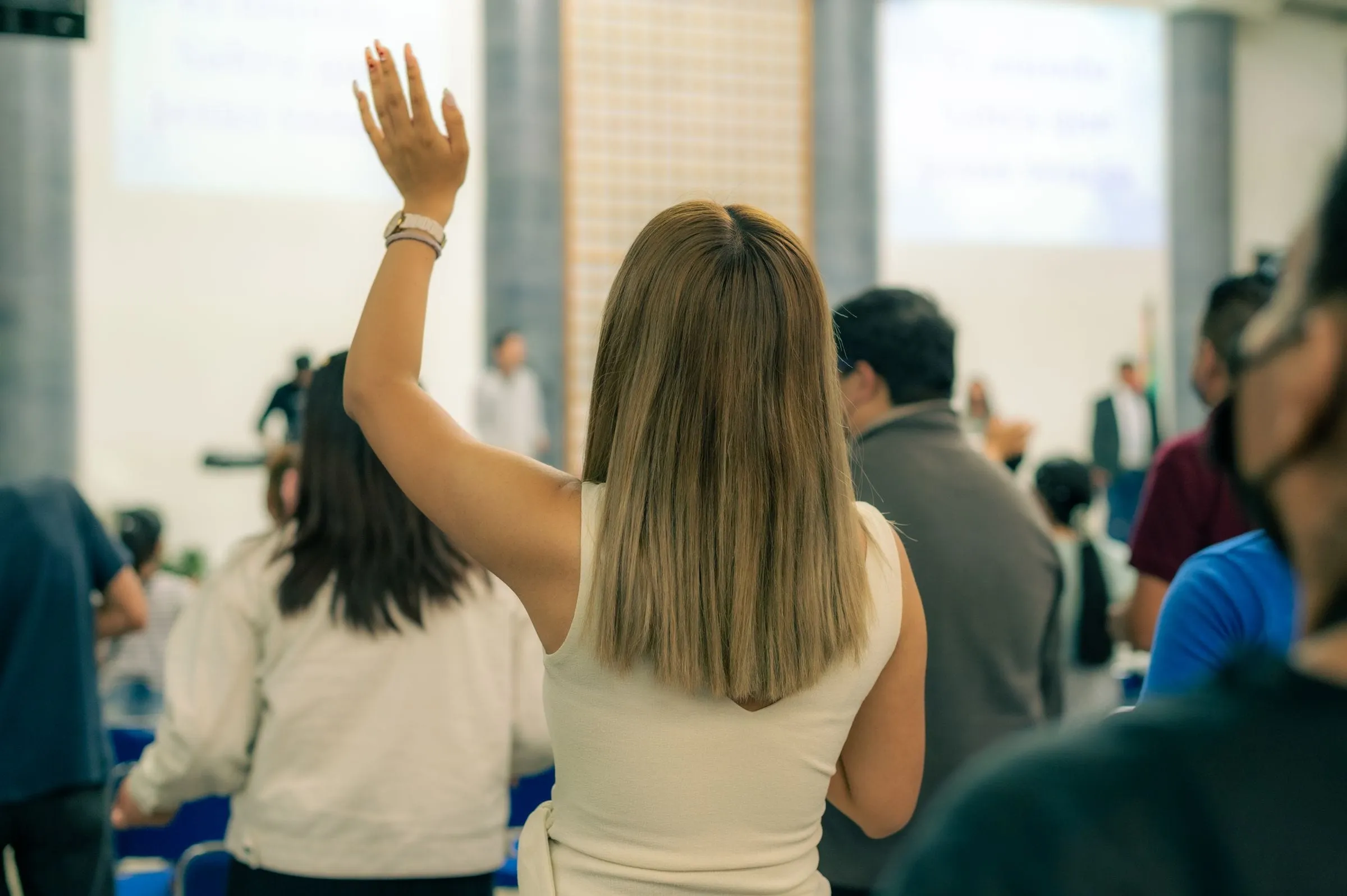 A woman in an audience raising her hand to ask a question