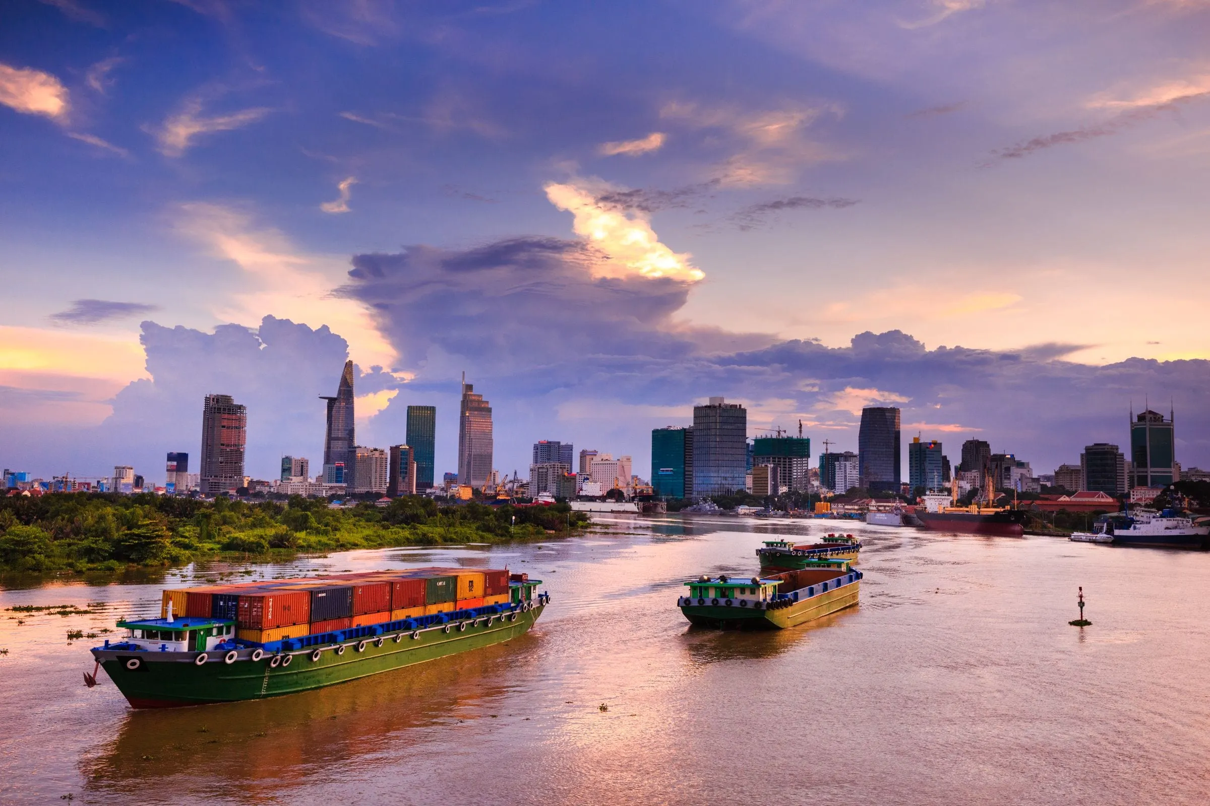 Container barges on the Saigon River with the Ho Chi Minh City skyline at dusk