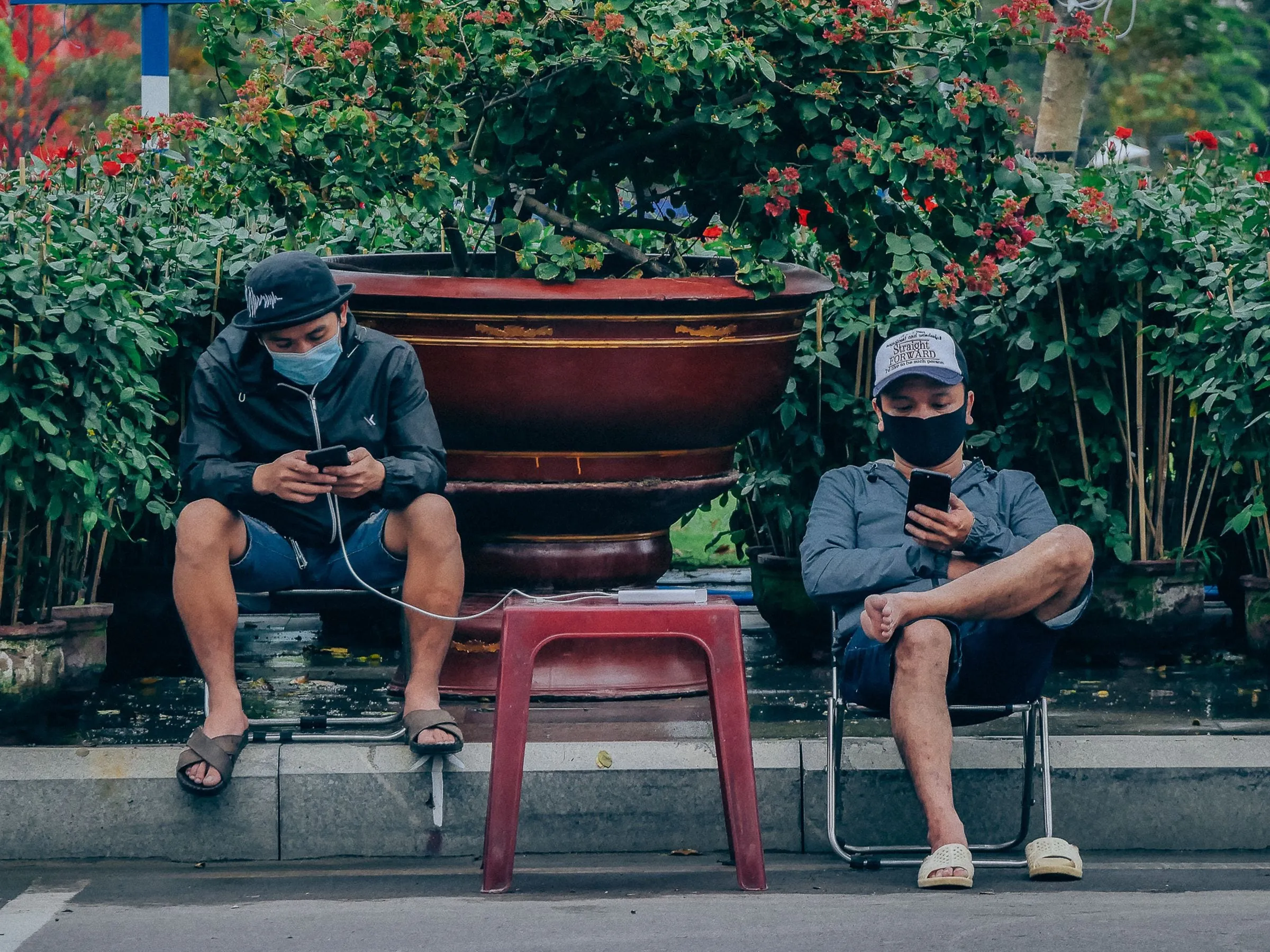 Two men in face masks using smartphones on a street in Quy Nhon, Vietnam