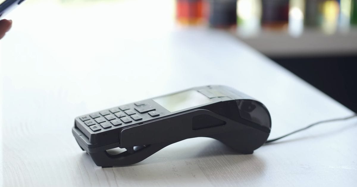 A hand tapping a smartphone on a card payment terminal