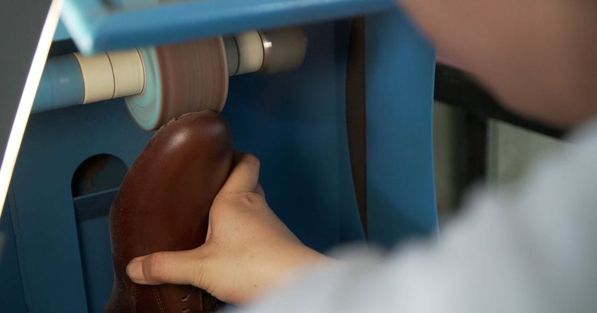 A worker holding a leather shoe against a buffing wheel in a shoe workshop